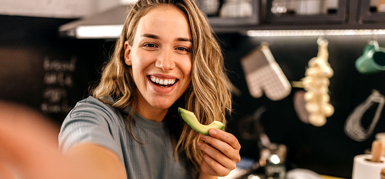 Een jonge vrouw lacht terwijl ze een avocado eet