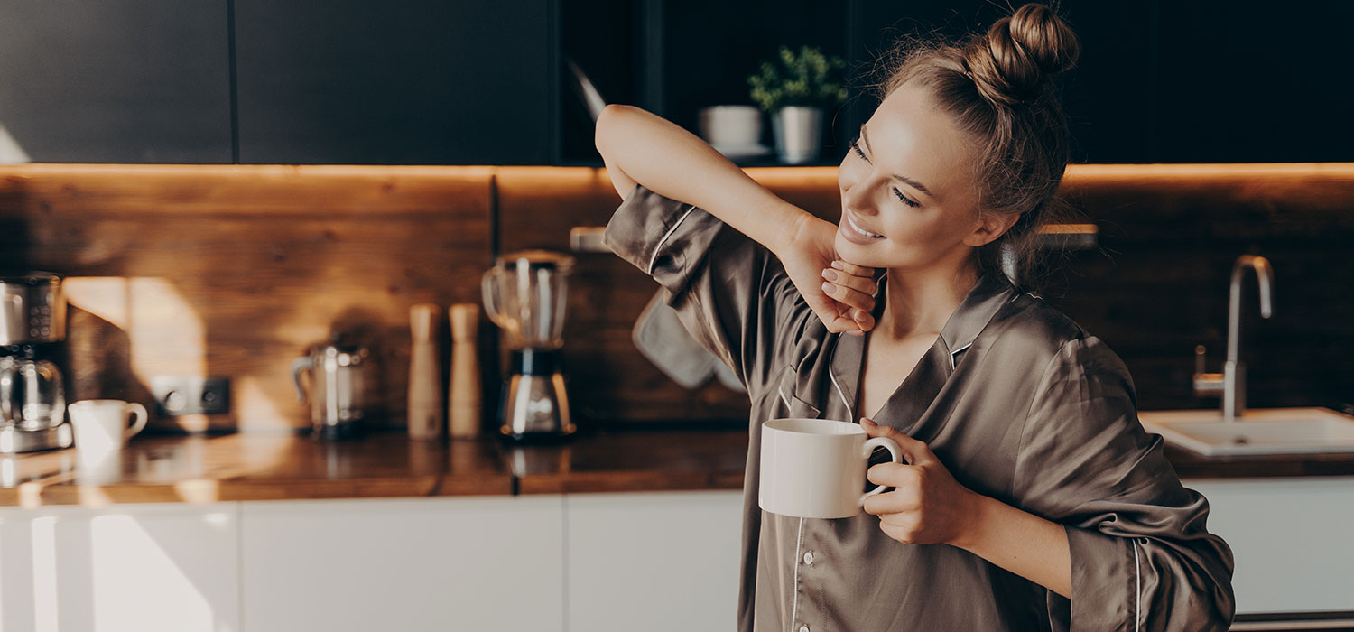 Vrouw drinkt koffie en rekt zich uit in haar keuken 
