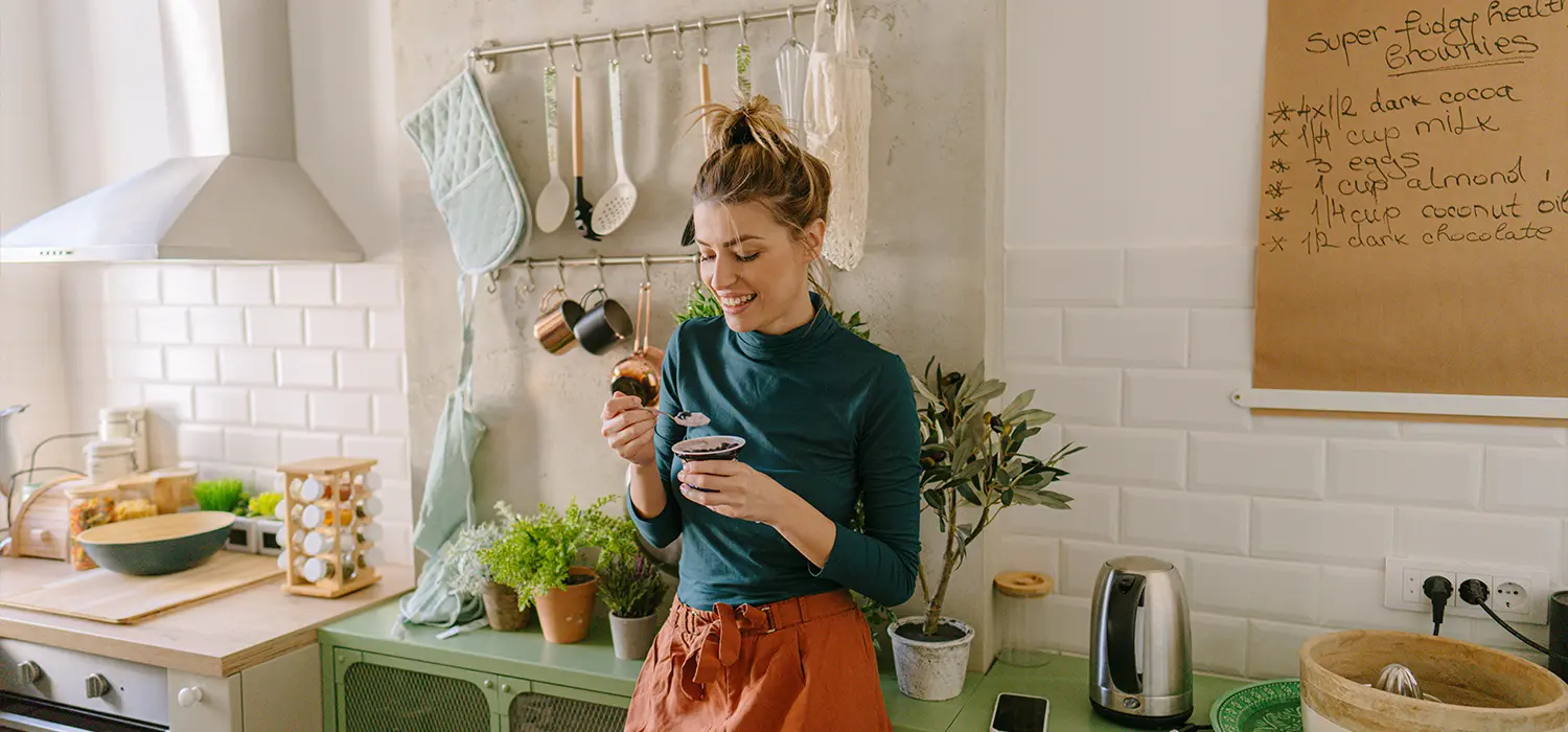 Vrouw die glimlachend staand in de keuken eet